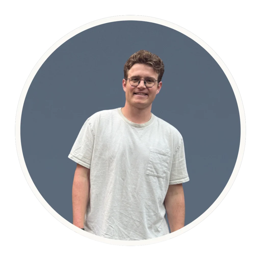 Dr. Luke Alley smiles in a striped t-shirt against a slate-blue background.