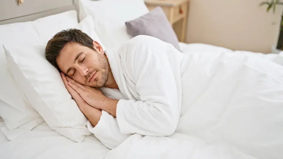 A man in a white robe sleeps peacefully on white pillows.